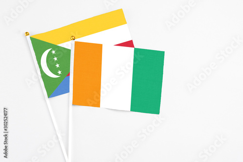 Cote D'Ivoire and Comoros stick flags on white background. High quality fabric, miniature national flag. Peaceful global concept.White floor for copy space.