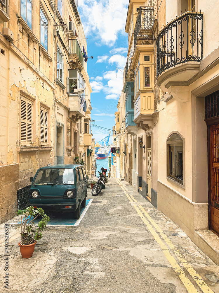 Traditional Maltese street in Valetta, Malta. Narrow street with car, sky, sea and marina view. Travel and tourism in Malta concept. Cityscape of Valletta. Architecture of Valetta.