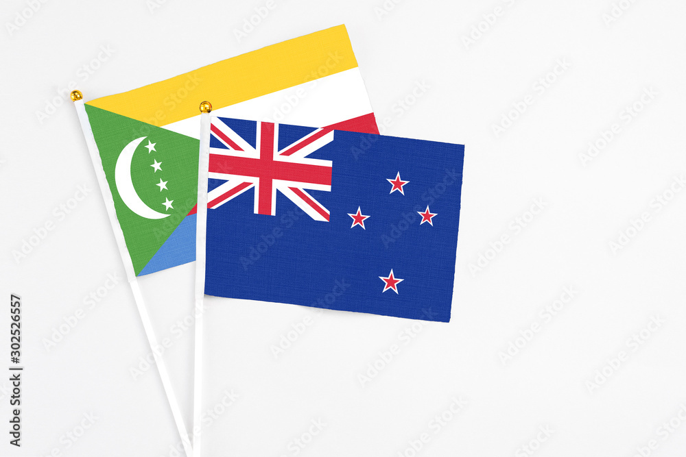 Fototapeta premium New Zealand and Comoros stick flags on white background. High quality fabric, miniature national flag. Peaceful global concept.White floor for copy space.