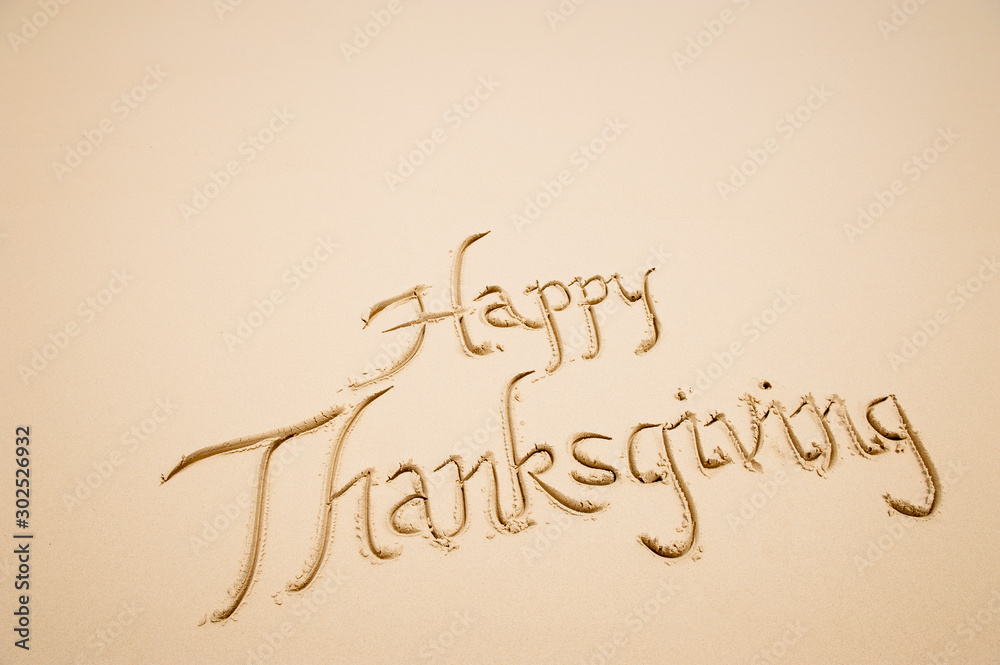 Happy Thanksgiving message handwritten in simple calligraphy script on smooth sand beach Happy Thanksgiving message handwritten in simple calligraphy script on smooth sand beach
