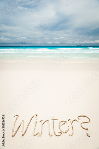 Cheeky Winter message handwritten on bright tropical beach lapped by turquoise waters