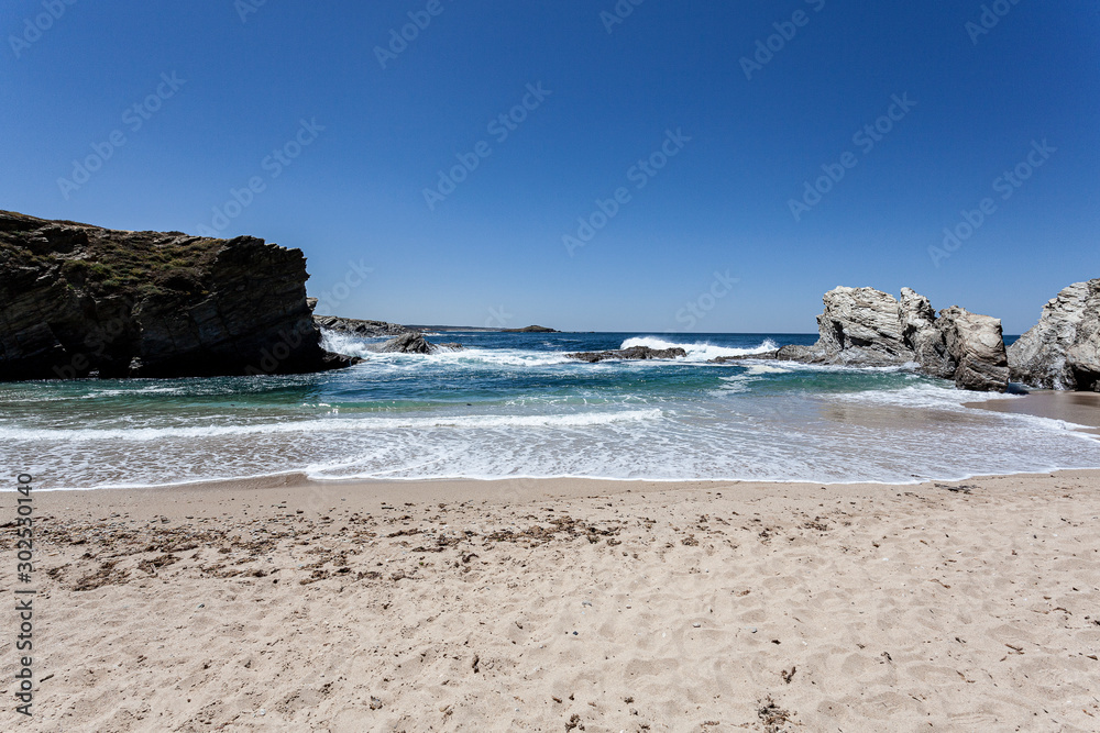 Ondas numa praia tranquila protegida das ondas do oceano pelas rochas.