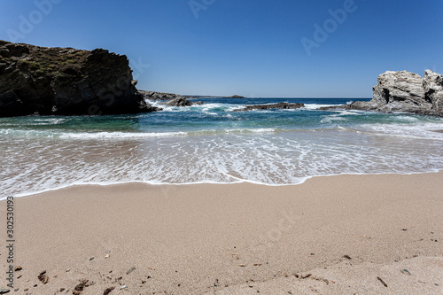 Ondas numa praia tranquila protegida das ondas do oceano pelas rochas.