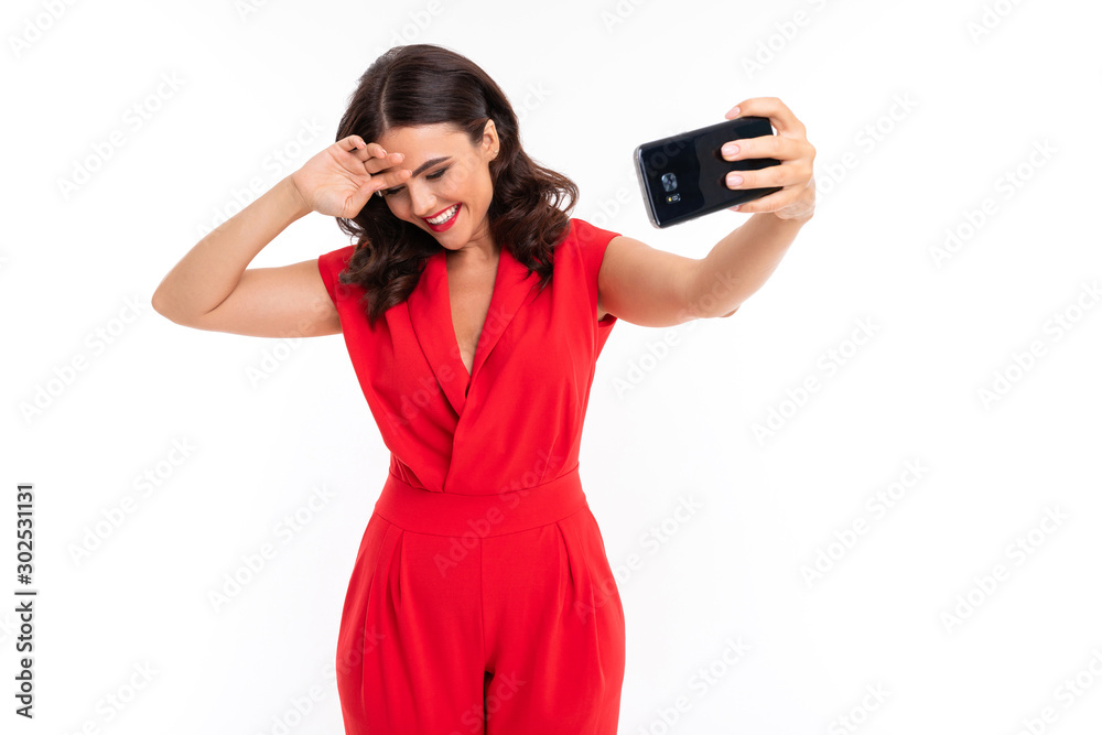 A young woman with bright makeup, in a red summer dress stands with a phone in hand A young woman with bright makeup, in a red summer dress stands with a phone in hand
