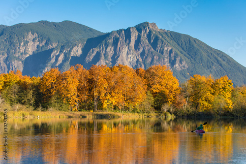SNOQUALMIE, WA, OCTOBER 24, 2017: A lone kayaker paddles across a large pond reflecting the beautiful fall colors of nearby trees and Mt. Si in the distant background.