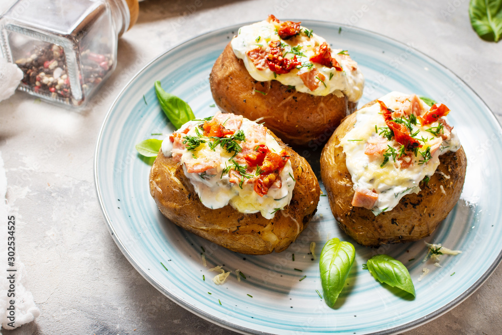 Baked stuffed potatoes with bacon, tomato, cheese on concrete background.