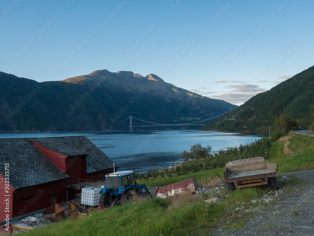 Fototapeta premium View on Hardanger Bridge across fjord Hardangerfjorden connects Ullensvang and Ulvikin, Norway. Longest tunnel to tunnel suspension bridge in the world 1380 meters. Summer day golden hour.
