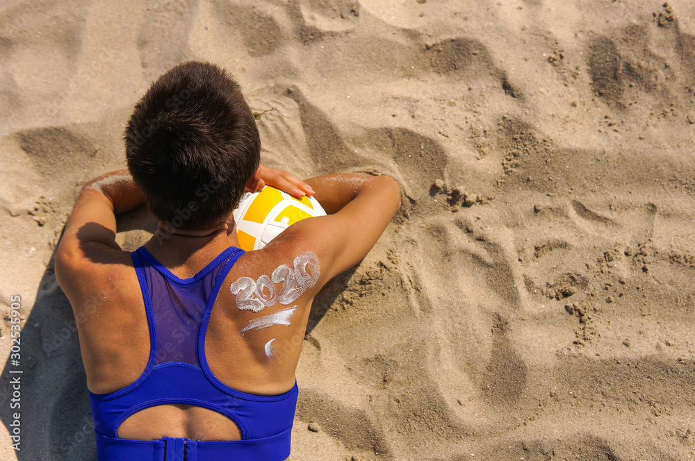 Christmas time spent at the beach in summer. Young woman wearing bikini with sunlotion 2020 on a shoulder Christmas time spent at the beach in summer. Young woman wearing bikini with sunlotion 2020 on a shoulder