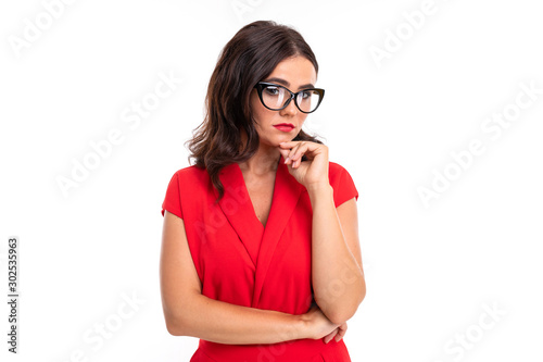 A young woman with bright makeup, in a red summer dress stands with a glasses and think about something serious