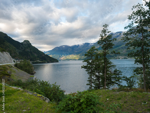 View over blue water of Hardanger Fjord in Kinsarvik in Norway with small village on the coast. Nature and travel background. Early autumn golden hour light.