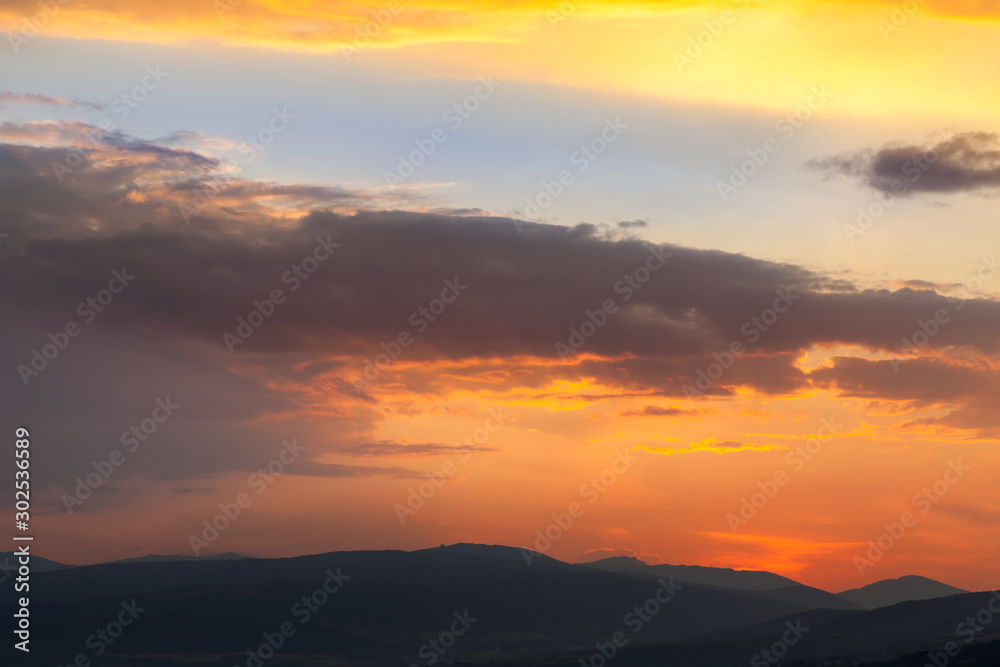 Amazing light on the cloud formations beautifully colored by sunset light and silhouettes of distant horizon mountains