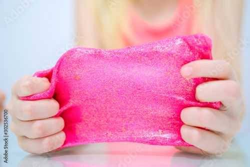 Blonde girl stretching pink glitter slime to the sides. Kids hands playing slime toy. Making slime. Copyspace. Selective focus. Mock up for text. photo