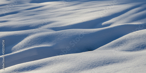 Abstract shapes in snow created by wind. Ice cold snow texture with long shadows, snow dunes. © doart