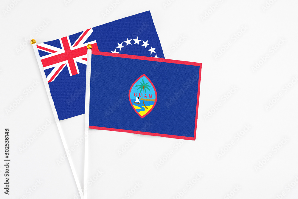 Fototapeta premium Guam and Cook Islands stick flags on white background. High quality fabric, miniature national flag. Peaceful global concept.White floor for copy space.
