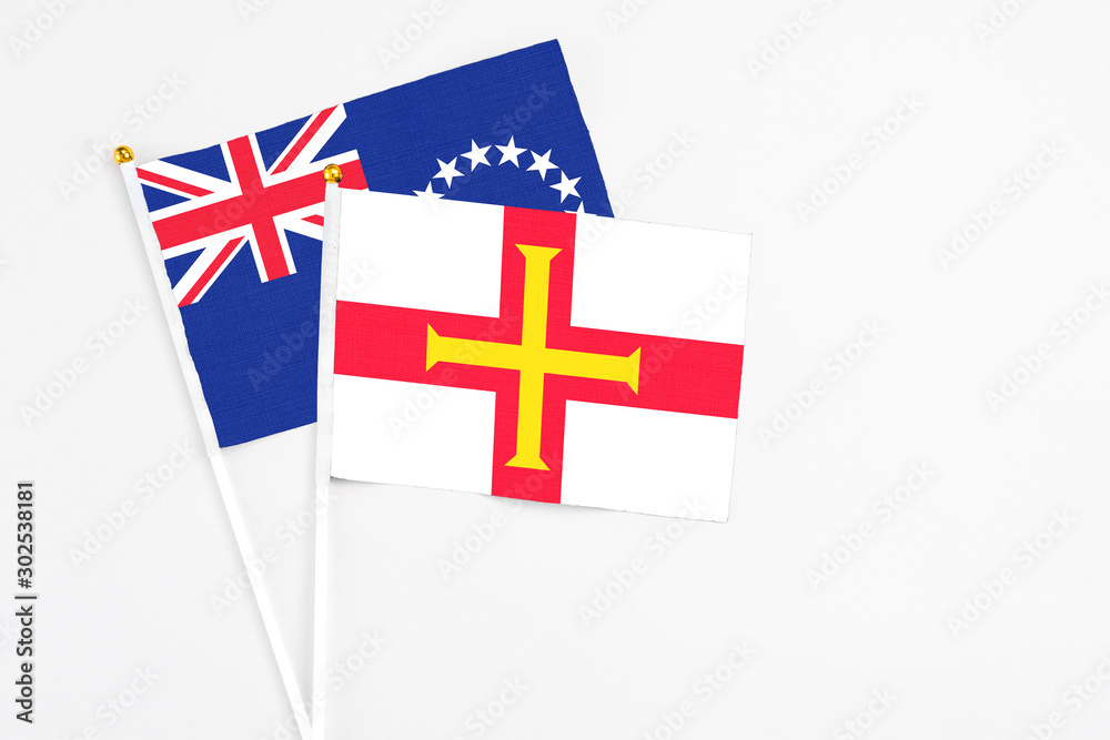 Guernsey and Cook Islands stick flags on white background. High quality fabric, miniature national flag. Peaceful global concept.White floor for copy space.