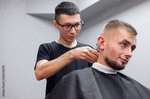 Uzbek hairdresser cuts a young handsome guy in a barbershop, a male client sits in a beauty salon and makes a short haircut