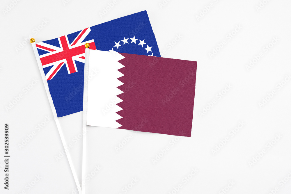 Fototapeta premium Qatar and Cook Islands stick flags on white background. High quality fabric, miniature national flag. Peaceful global concept.White floor for copy space.