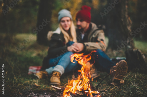 Traveler couple camping in the forest and relaxing near campfire after a hard day. Concept of trekking, adventure and seasonal vacation.