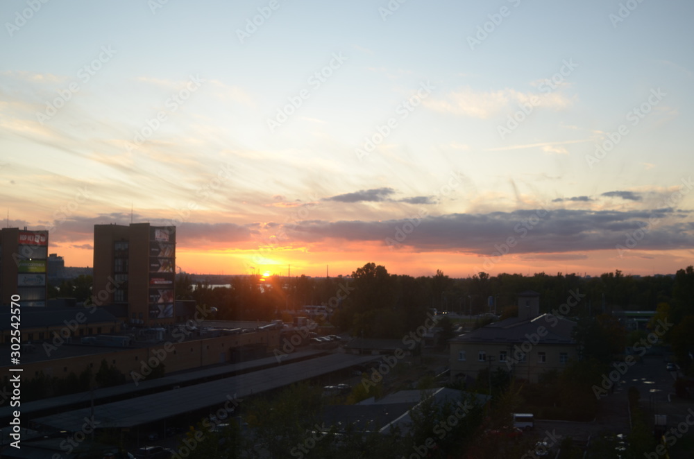 View of the dramatic sky above the sity at sunset with dark blue clouds and pink, purple and yellow flashes from the sun's rays View of the dramatic sky above the sity at sunset with dark blue clouds and pink, purple and yellow flashes from the sun's rays