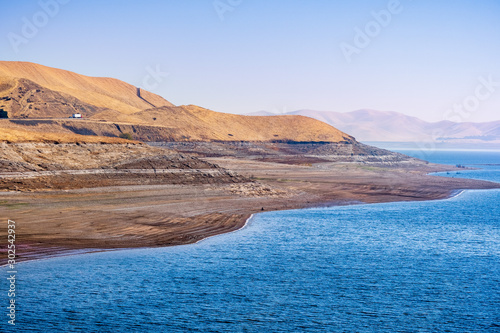 The shoreline of San Luis Reservoir, an artificial lake storing water for agricultural purposes in Central California; visible low water level towards the end of fall; Merced County, California; photo