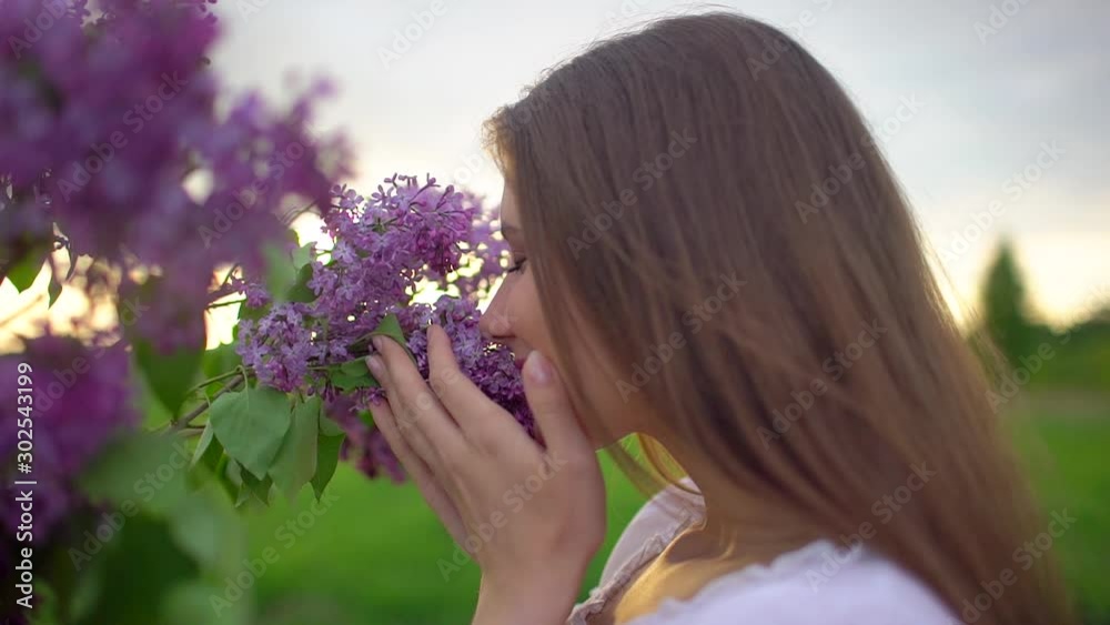 Young romantic smiling beautiful woman girl sniffing smelling lilac flowers in bouquet in nature outdoors, Inhaling aroma of flowers enjoying smell fragrance perfume freshness spring summer Beauty