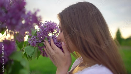 Young romantic smiling beautiful woman girl sniffing smelling lilac flowers in bouquet in nature outdoors, Inhaling aroma of flowers enjoying smell fragrance perfume freshness spring summer Beauty