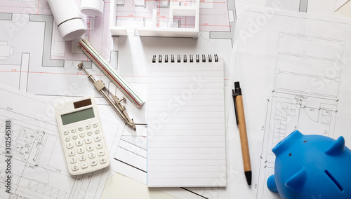 Construction cost concept. Engineer office desk, blue piggy bank, calculator and blank notepad on drawings