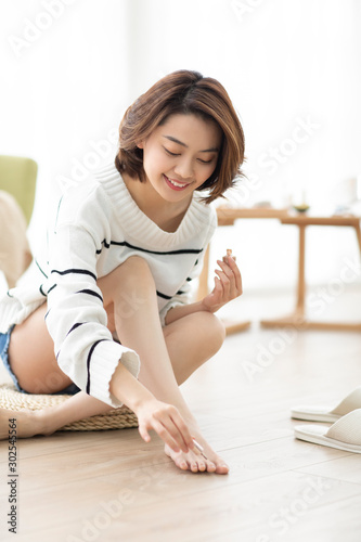 Happy young Chinese woman applying nail polish at home photo