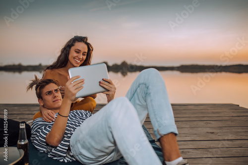 Young couple watching videos or sharing media content from a tablet, while sitting by the river © Jovica Varga