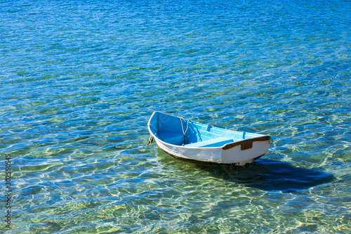 Photography A small blue and white wooden row boat anchored in shallow calm clear water on a sunny summer day
