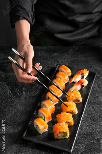 Woman eating tasty sushi on dark background