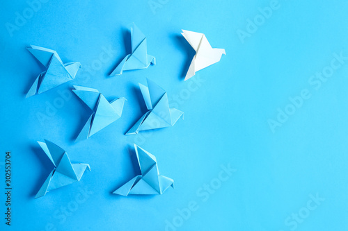 White origami bird among blue ones on color background. Concept of uniqueness