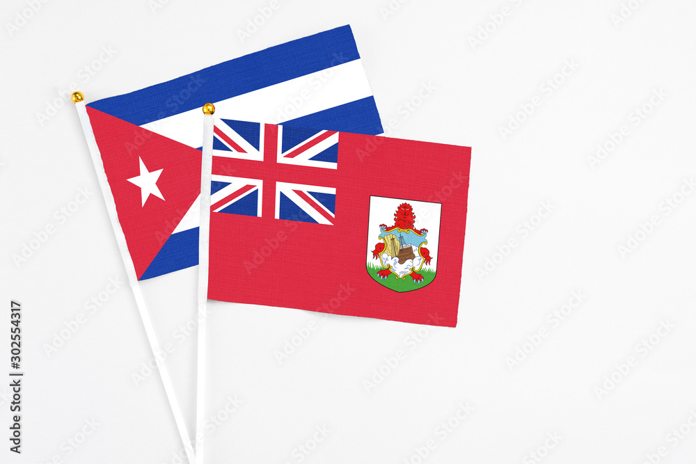Fototapeta premium Bermuda and Cuba stick flags on white background. High quality fabric, miniature national flag. Peaceful global concept.White floor for copy space.