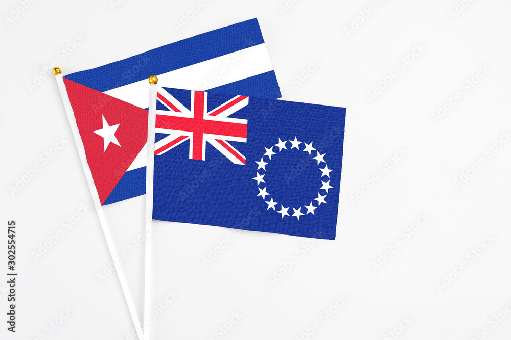 Fototapeta premium Cook Islands and Cuba stick flags on white background. High quality fabric, miniature national flag. Peaceful global concept.White floor for copy space.