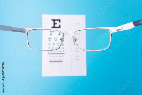 Hand-held glasses, view of the Snellen chart. Eye examination. Blue background