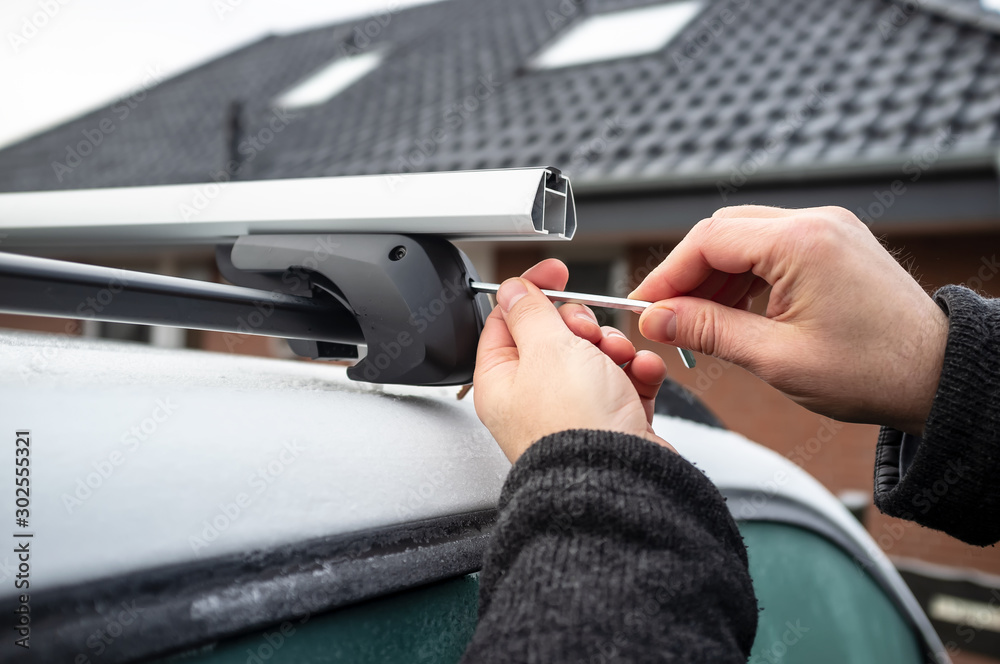 Man with a screwdriver installs attachments for trunk or cargo box on roof of the car.