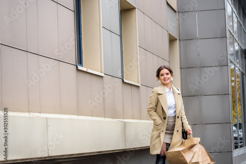 Young woman at the street with shopping bags. Beautiful emotional girl in a coat. Black friday sale concept. Street photo in the metropolis.