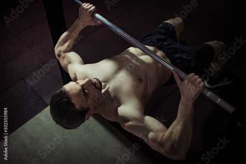 Athlete muscular fitness male model pulling up on horizontal bar in a sport-club.