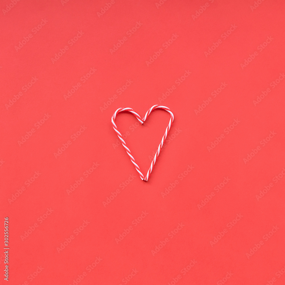 Christmas candy cane in a shape of heart, Valentine's day concept. Red background, flat lay.
