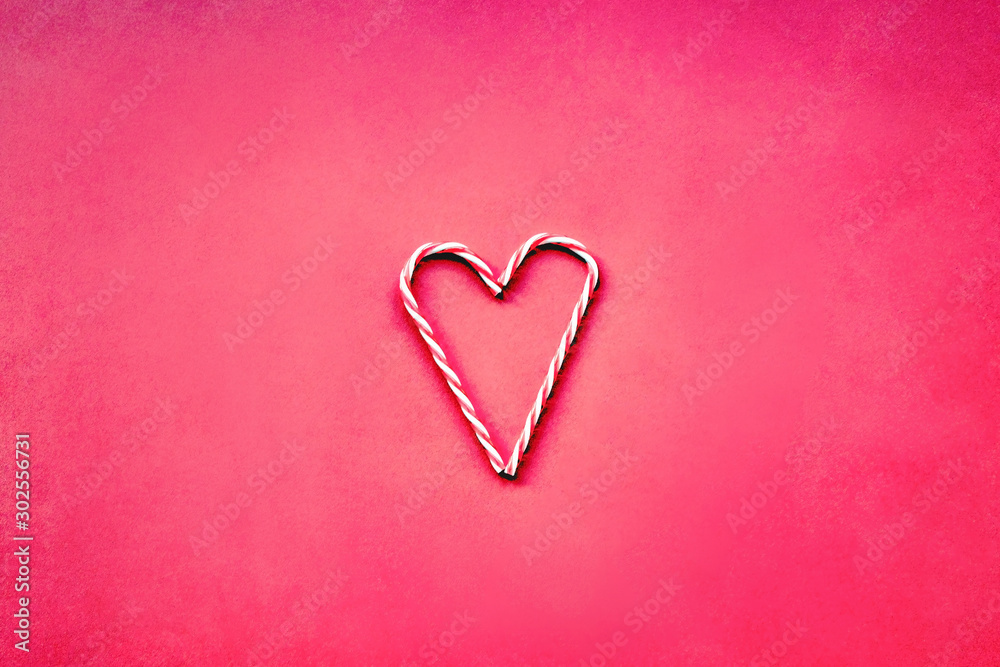 Christmas candy cane in a shape of heart, Valentine's day concept. Red background, flat lay.