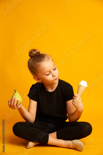 Puzzled little dancer choosing between pear and ice cream