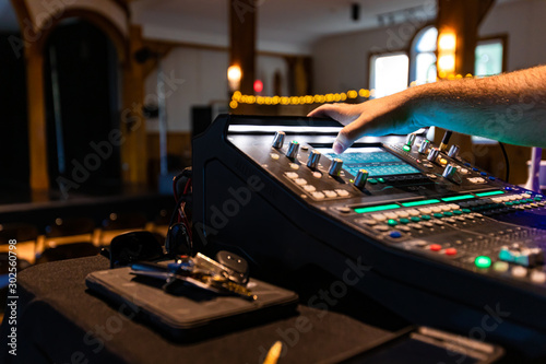Selective focus photo of a person setting up lighting and music settings at a concert hall with bokeh lights on the top