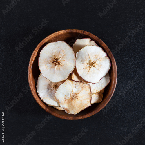 Dried Apple chips in a wooden bowl on a black stone background. Organic natural food.