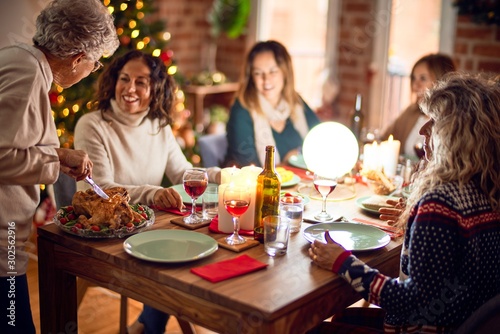 Beautiful group of women smiling happy and confident. Carving roasted turkey celebrating christmas at home