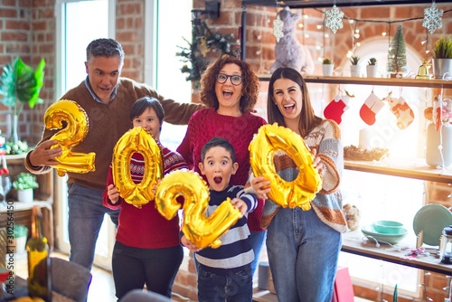 Beautiful family smiling happy and confident. Standing and posing holding 2020 balloons celebrating new year at home