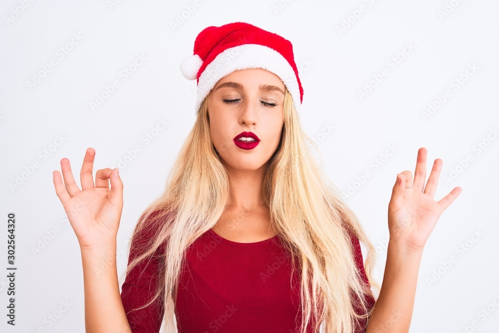 Young beautiful woman wearing Christmas Santa hat over isolated white background relax and smiling with eyes closed doing meditation gesture with fingers. Yoga concept. Young beautiful woman wearing Christmas Santa hat over isolated white background relax and smiling with eyes closed doing meditation gesture with fingers. Yoga concept.