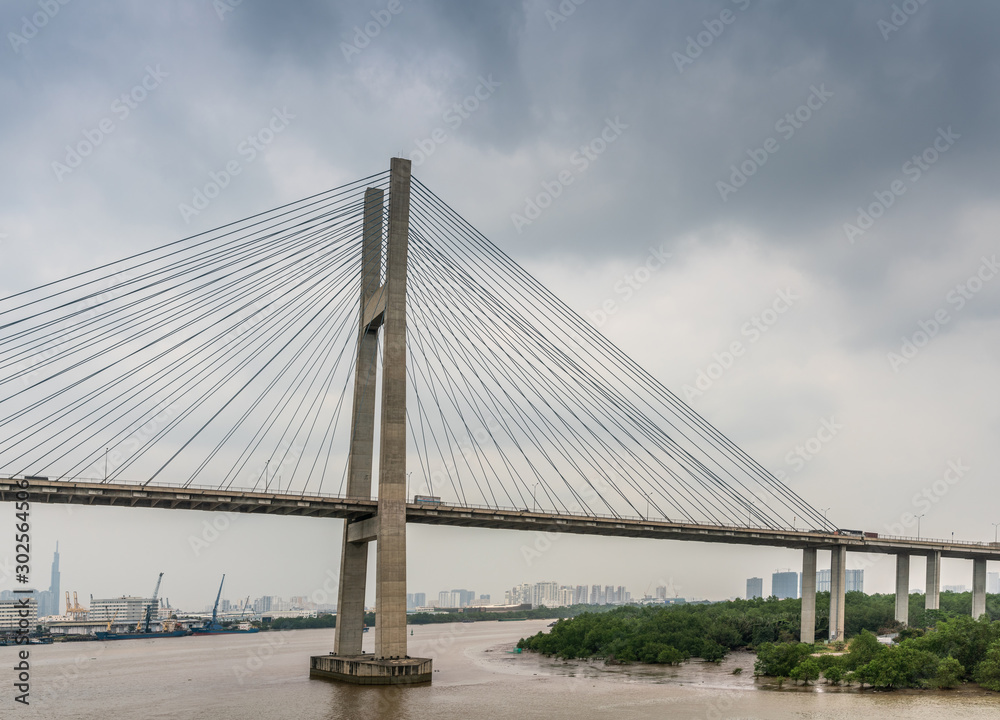 Ho Chi Minh City, Vietnam - March 12, 2019: Long Tau and song Sai Gon rivers meeting point. Landscape with  H-shaped pylon of Phu My suspension bridge in center under gray cloudscape. Brown water.