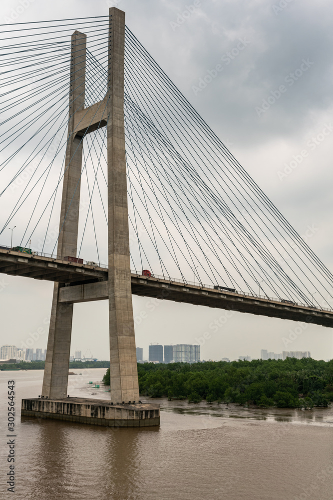 Naklejka premium Ho Chi Minh City, Vietnam - March 12, 2019: Long Tau and song Sai Gon rivers meeting point. Closeup of H-shaped pylon of Phu My suspension bridge under gray cloudscape. 
