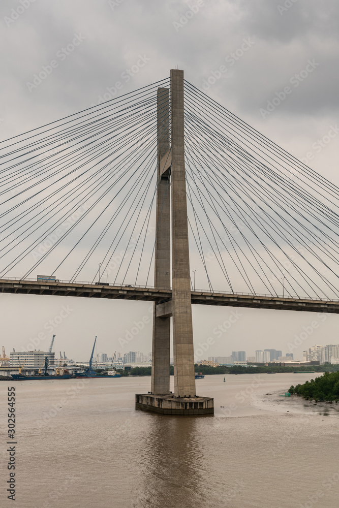 Ho Chi Minh City, Vietnam - March 12, 2019: Long Tau and song Sai Gon rivers meeting point. Closeup of  H-shaped pylon of Phu My suspension bridge under gray cloudscape. 