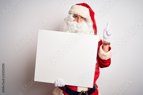 Middle age man wearing Santa Claus costume holding banner over isolated white background very happy pointing with hand and finger to the side © Krakenimages.com
